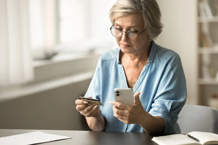 Mature woman sat at the desk with her mobile phone and credit card in hand.