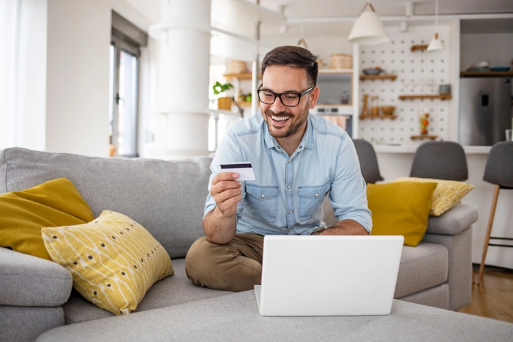 Happy man at home, using laptop and looking at credit card