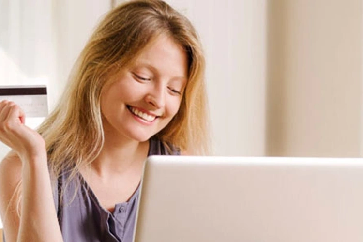 woman holding credit card while looking at laptop