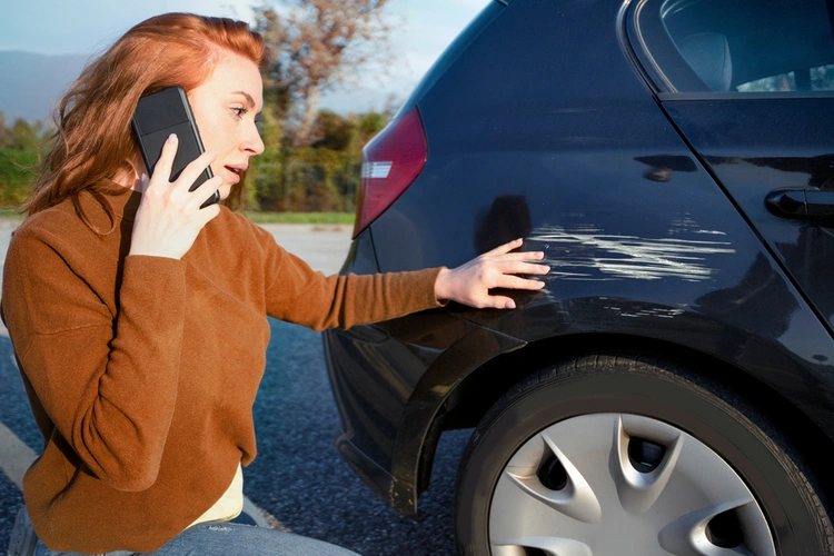 Woman on the phone whilst looking at a scrape on her car.