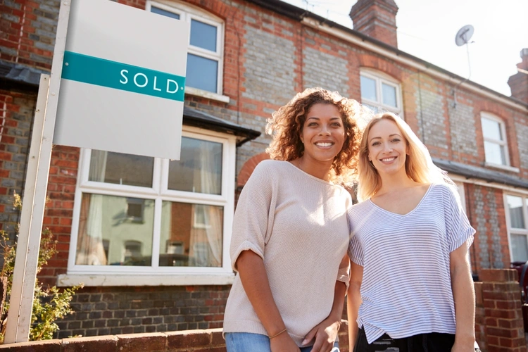 Two women stood outside the front of a house next to a sold sign