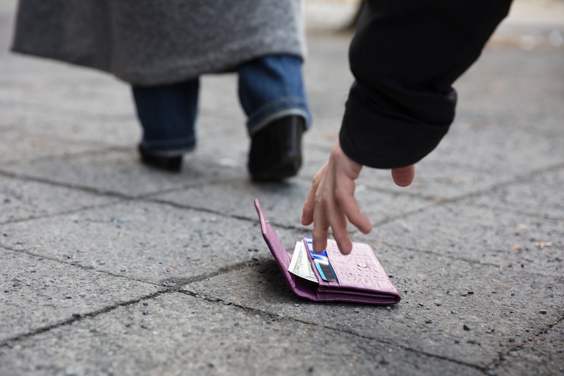Person picking up a dropped open purse off the road showing credit cards
