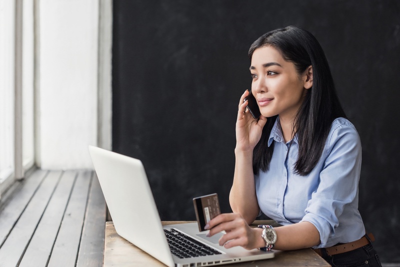 Woman at a laptop on phone making a credit card payment