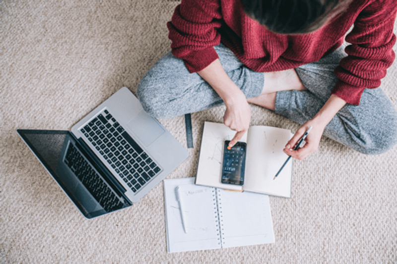 Woman sat on bedroom floor with laptop, calculator and documents
