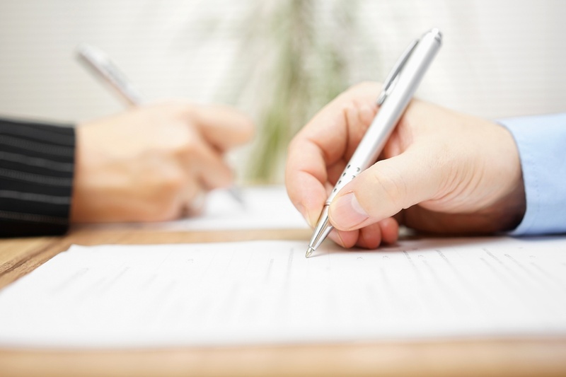 Two hands holding pens signing contracts