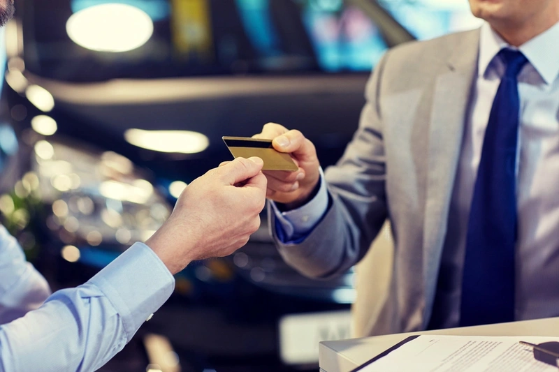 Business man handing a credit card over with a car in the background