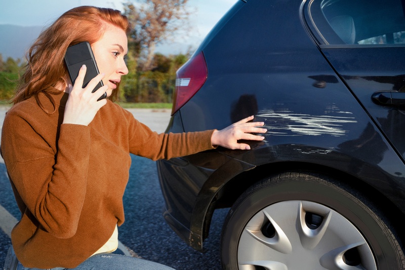 Woman on the phone whilst looking at a scrape on her car.
