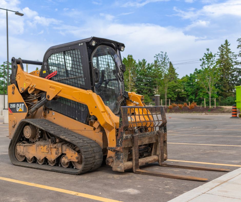 Cat compact track loader with fork attachments sitting idle in a parking lot