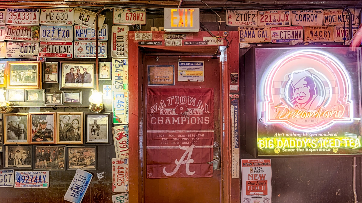 A photo of the inside of Dreamland BBQ filled with various license plates on the walls, framed photos, and a door with a "National Champions" banner on it.
