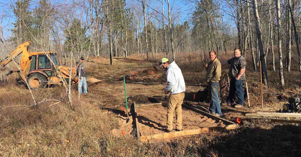 Group of men working in winter woods setting a frame for a disc golf tee pad