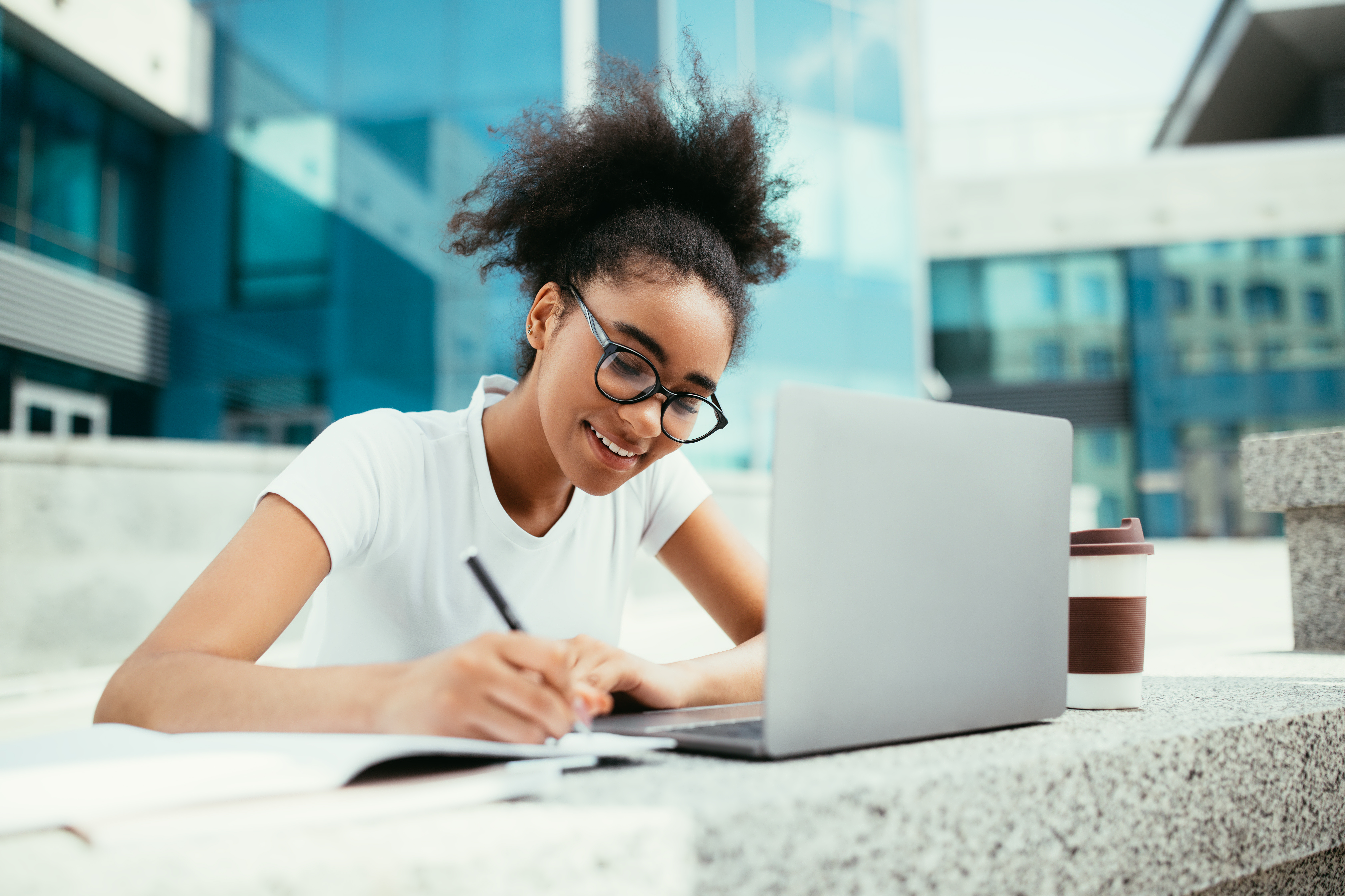 african american woman working at her computer and writing in a building courtyard