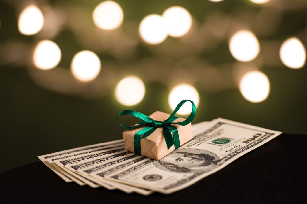 A small gift sits on top of money to represent setting a holiday budget.