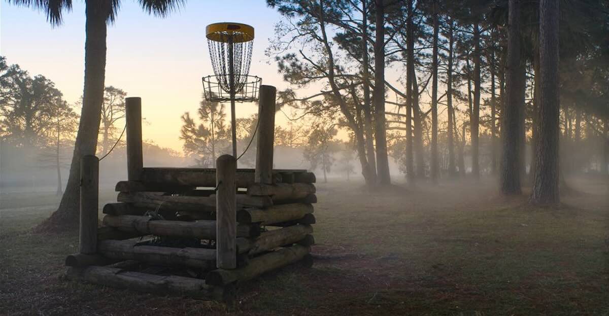 An elevated disc golf basket with a rustic wooden staircase up to it and a misty morning