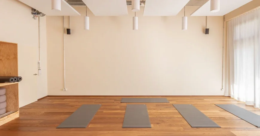 Lichtdurchflutetes Yoga-Studio mit Holzboden, großen Fenstern und natürlichen Materialien wie Holz und Leinen, das eine ruhige Atmosphäre schafft.