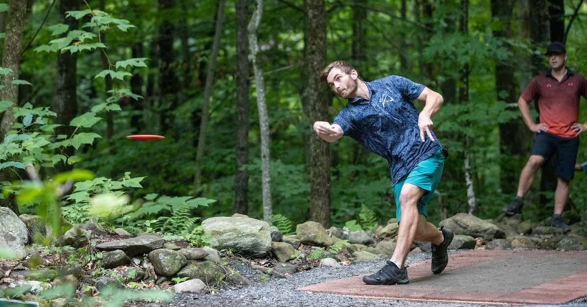 A young man throws a forehand shot from a paver tee in the woods