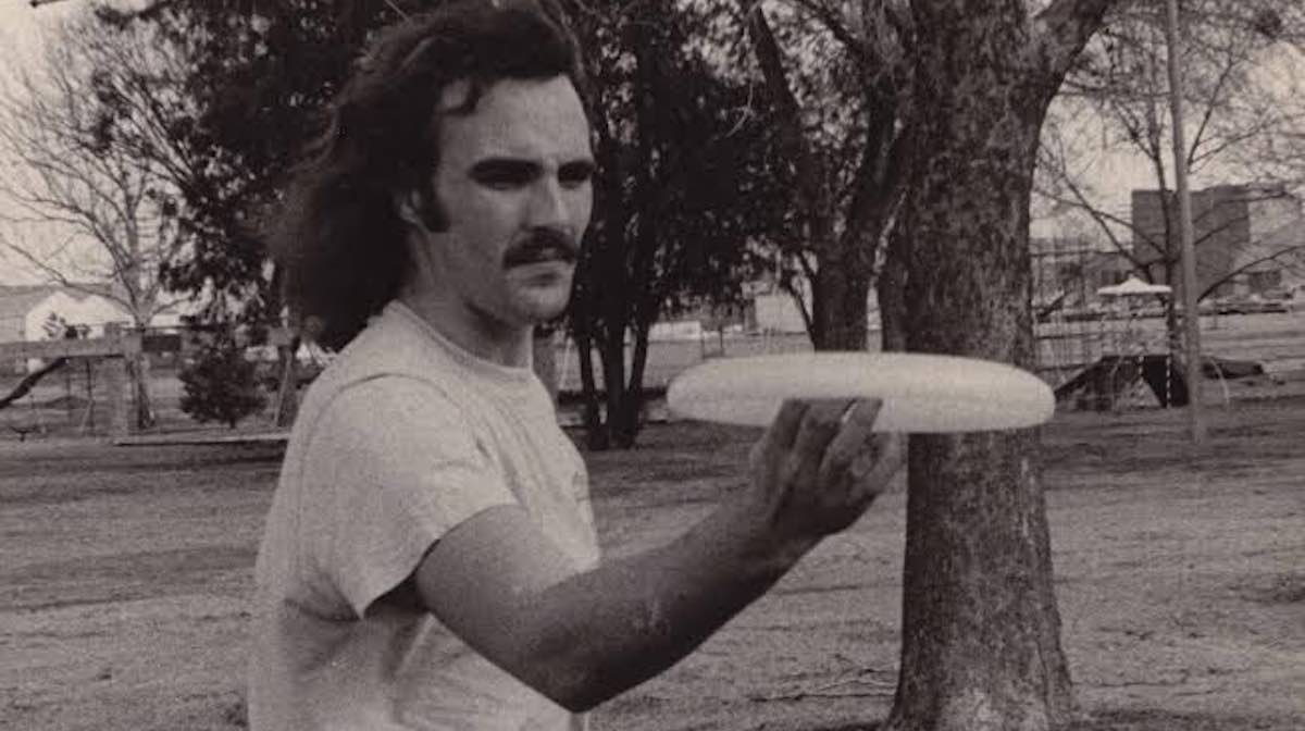 A black and white photo of man in retro attire spinning a Frisbee-like disc on his finger