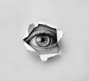 ripped hole in paper with person's eye looking through