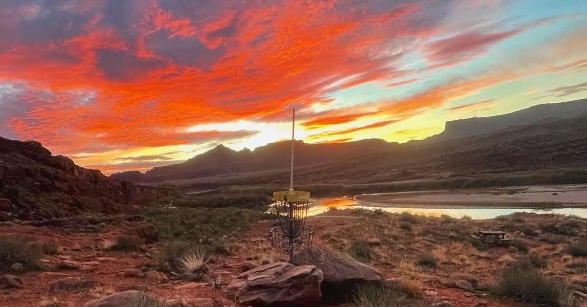 A yellow-banded disc golf basket in a red rock desert at either sunrise or sunset