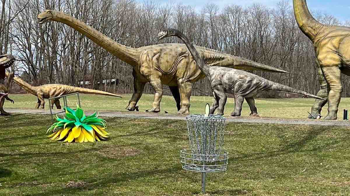 Life-size models of sauropods behind disc golf basket