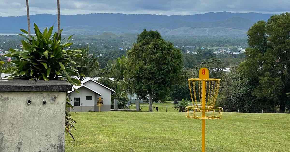Disc golf basket painted entirely yellow with city and mountains in the distance