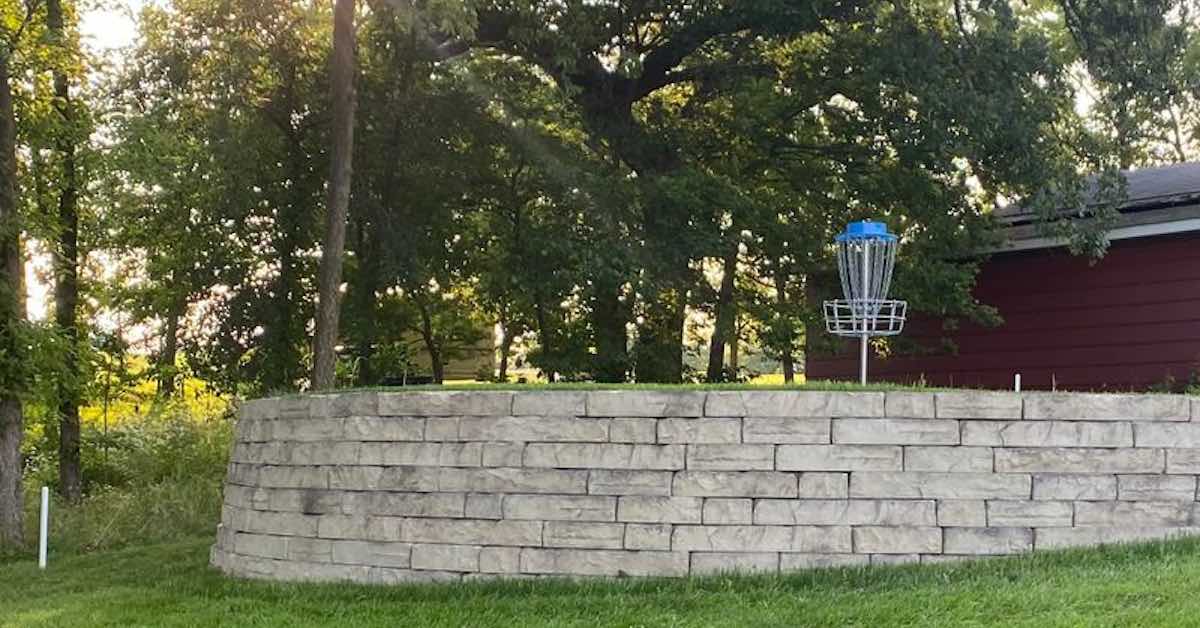 Disc golf basket on elevated surface surrounded by a stone wall