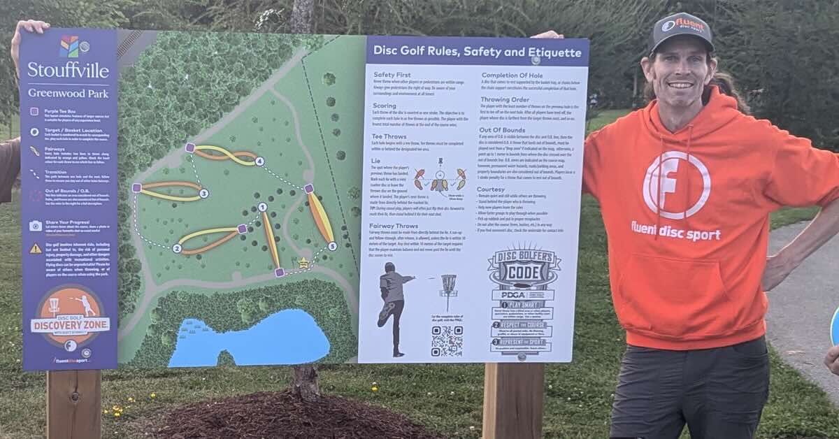  Man in an orange hoodie next to a disc golf course information board