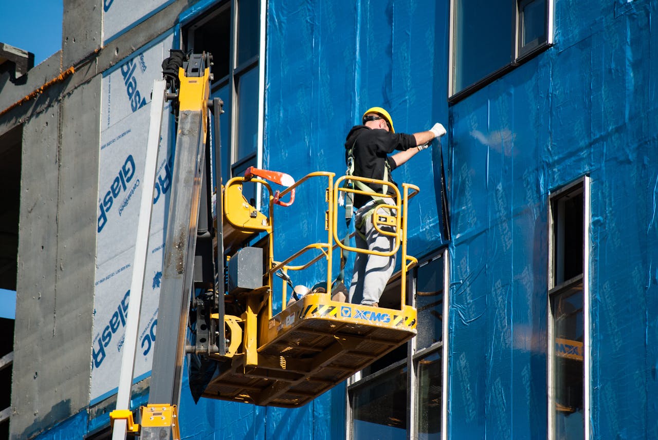 A photo of a construction site with a worker installing exterior insulation on a building.