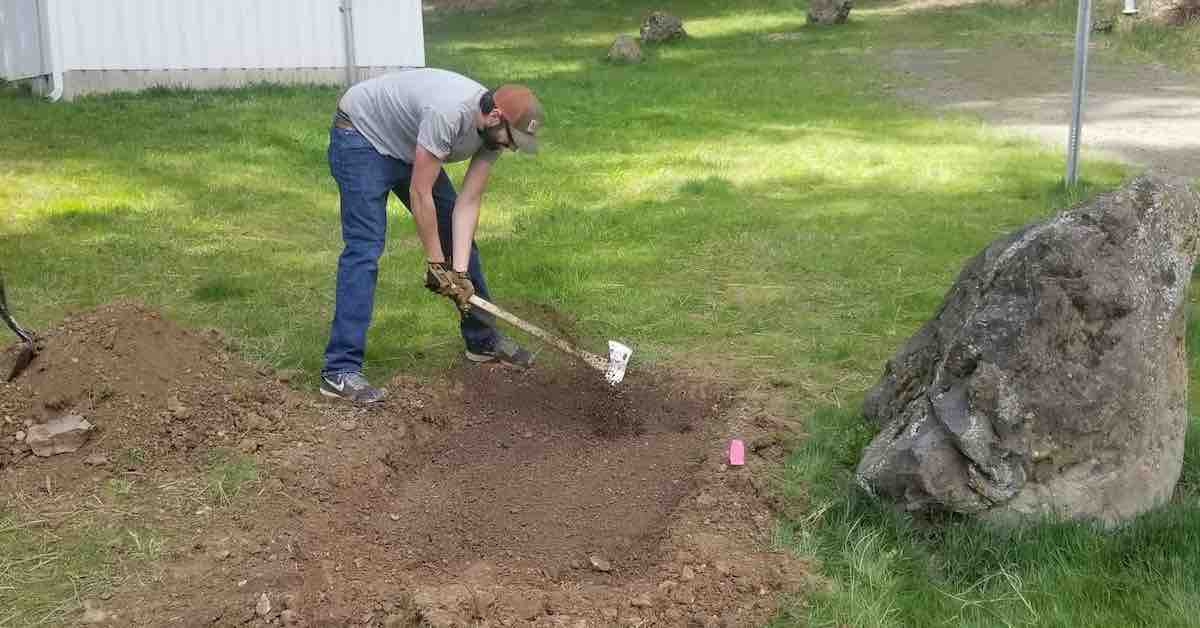 A man uses back of an axe to flatten dirt
