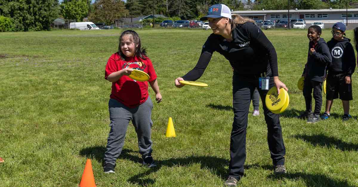 A woman in a field showing a young girl how to putt a disc golf disc