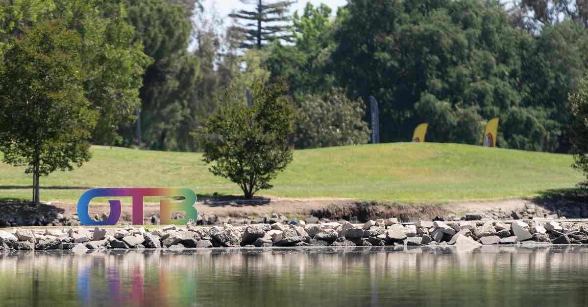 "OTB" sign in large, multicolored letters near a lake in a golf course setting