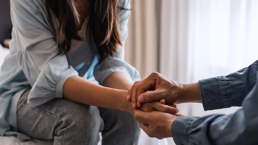Close-up of two people sitting together and holding hands in a supportive, comforting moment.