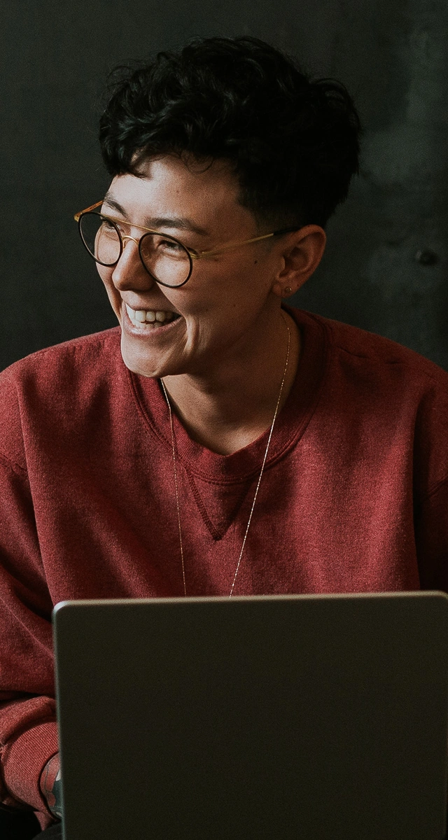 Person with short hair and glasses smiling while using laptop.