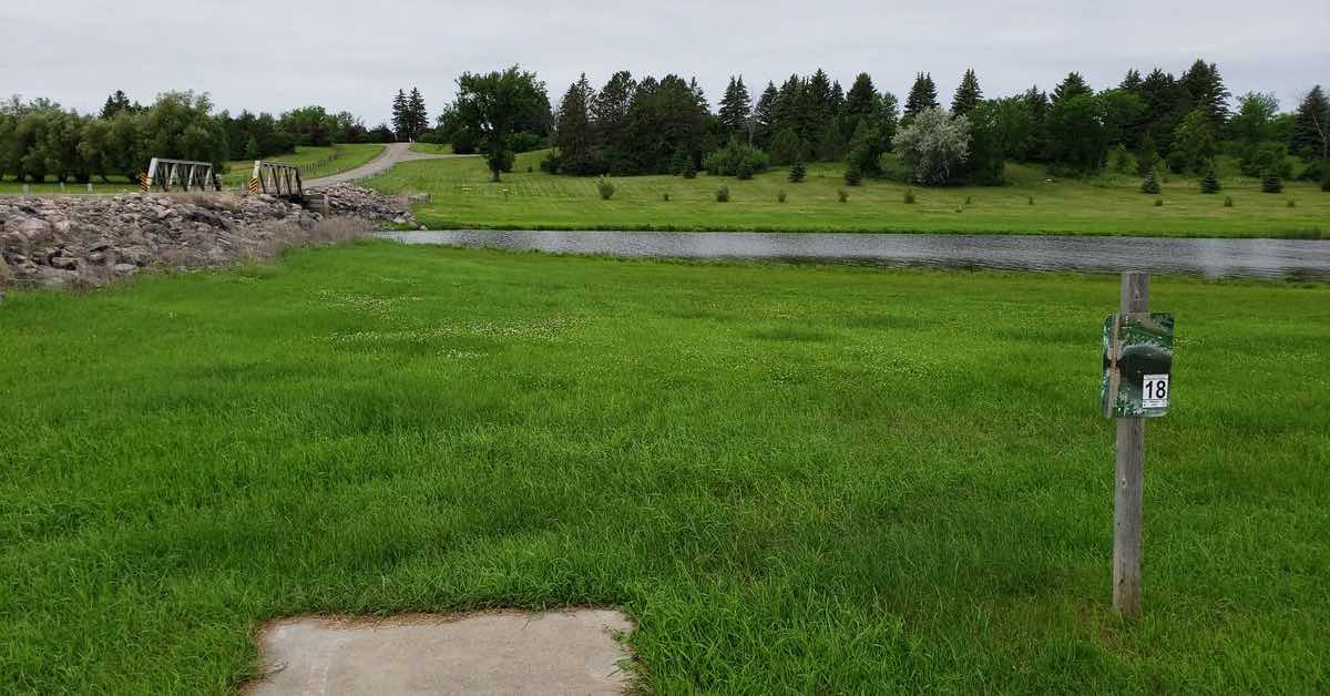 Concrete disc golf tee pad in green grass with a bridge and body of water int he distance