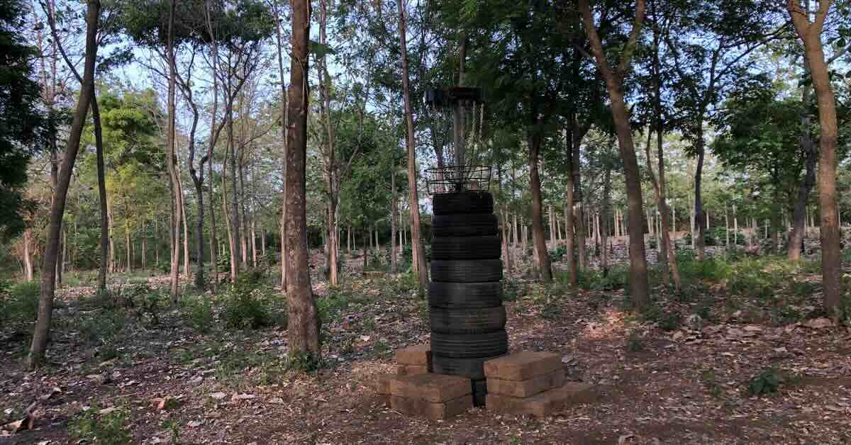A disc golf basket mounted on a tower of tires in an area of trees