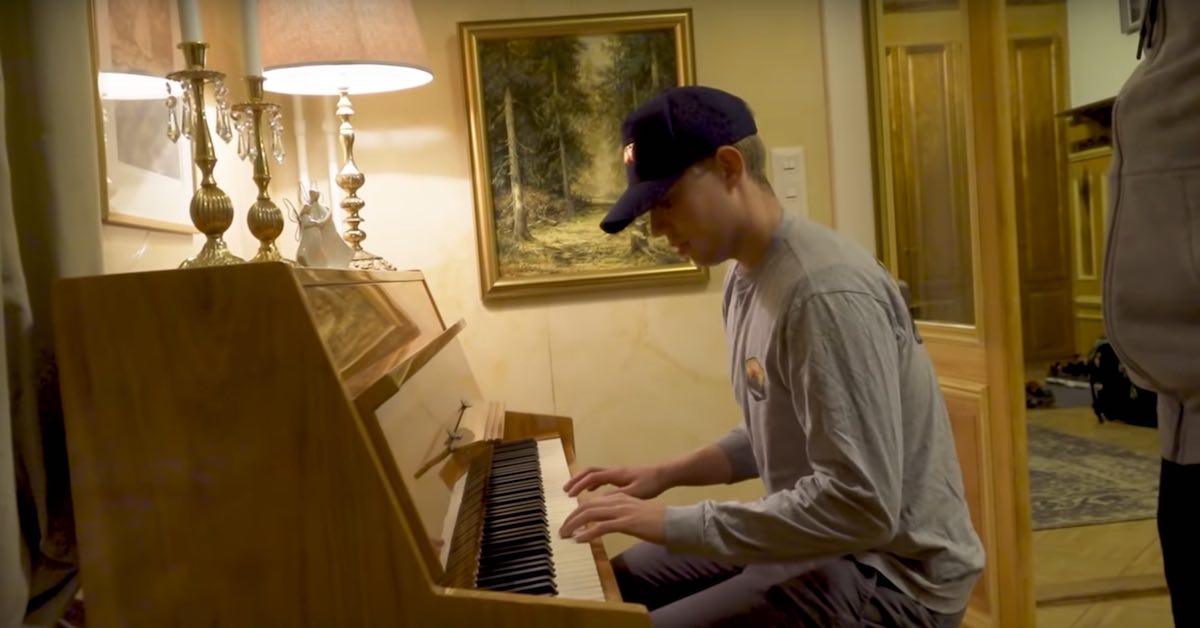 A young man with a ball cap on sits at a piano