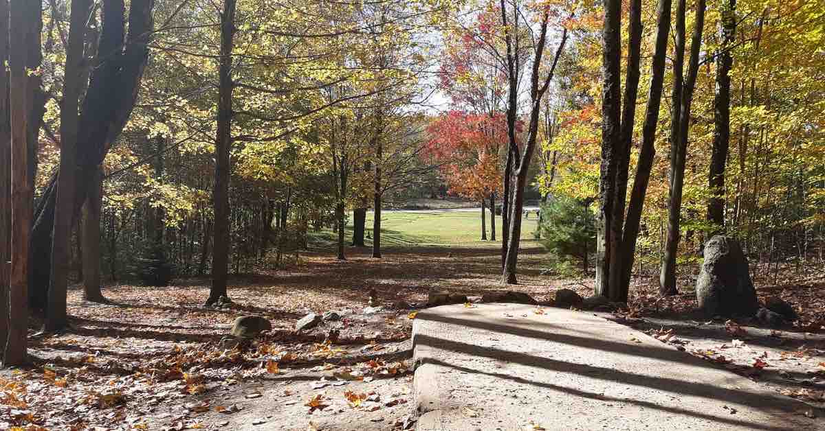 A disc golf tee pad at the start of downward-sloping fairway that leads to an open field some distance forward