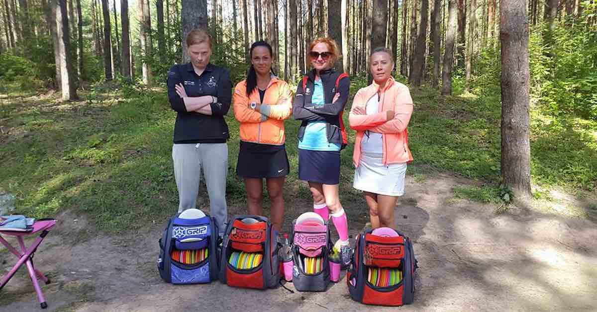 4 women with disc golf bags on a wooded course