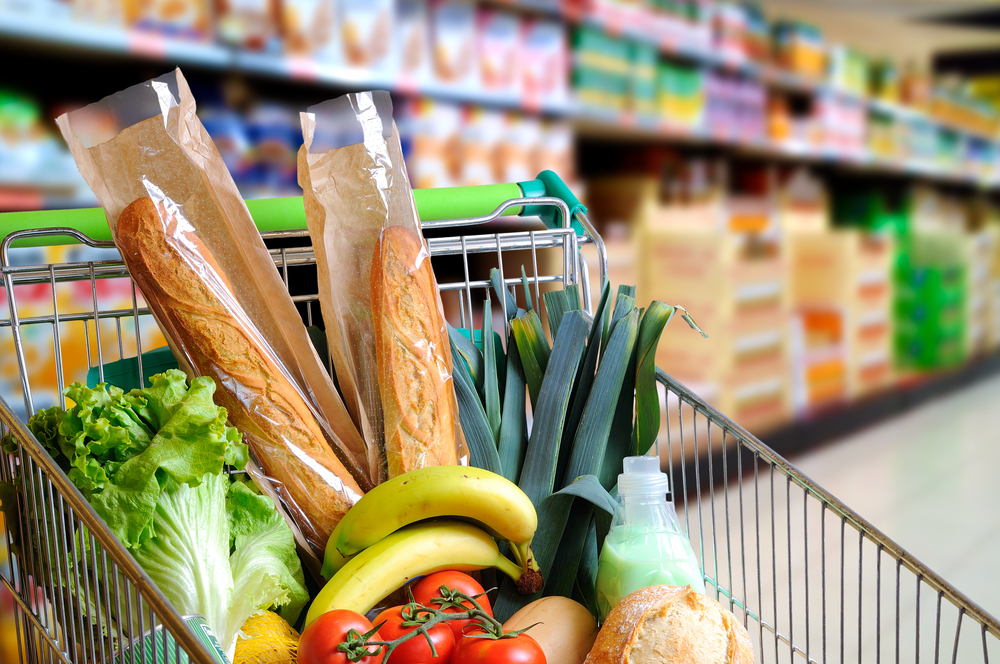 supermarket trolley with green handle filled with groceries including bananas, bread and greens