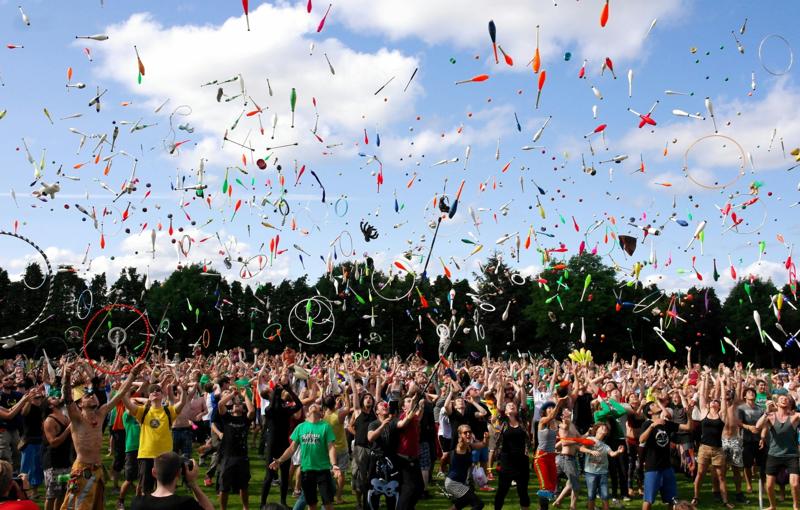 Large crowd at outdoor event with juggling props in the air.