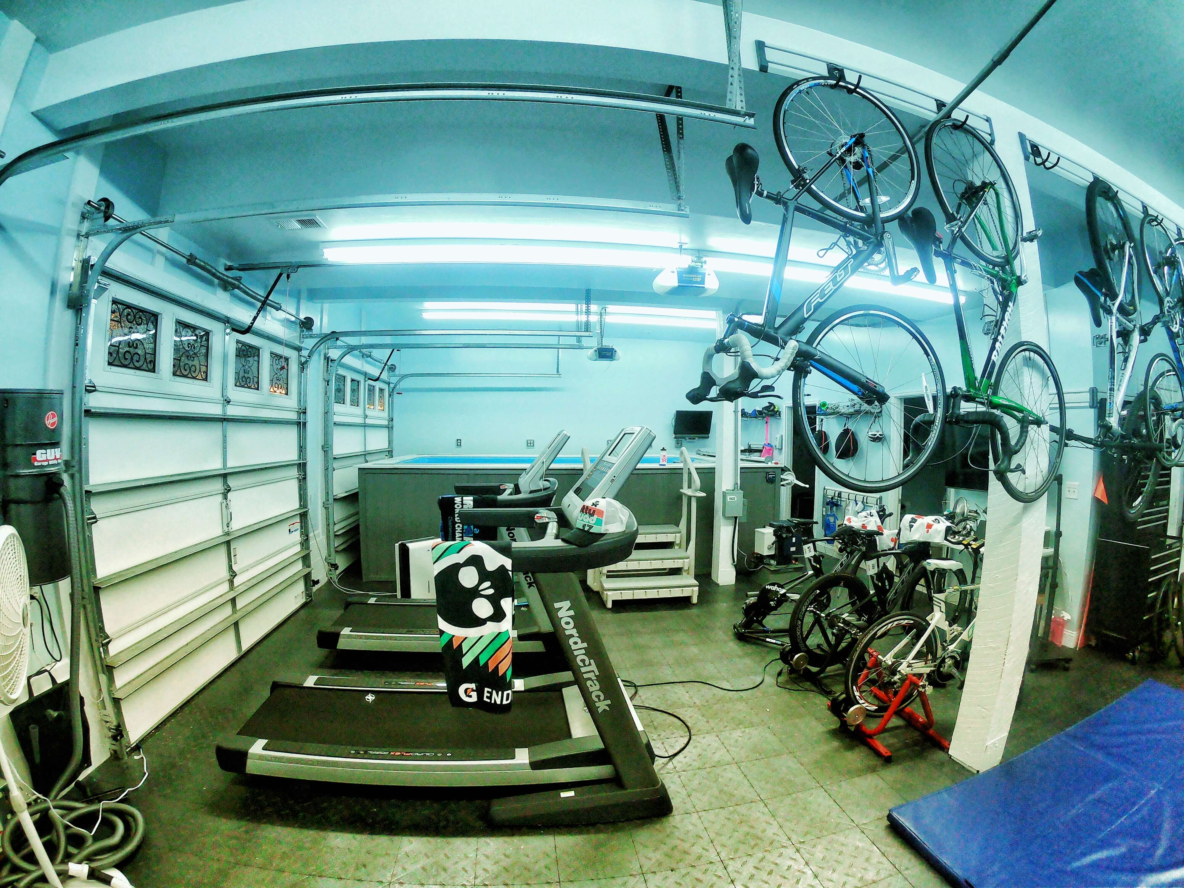 A family's garage 'pain cave' with aboveground Endless Pool, treadmills, and bicycles.