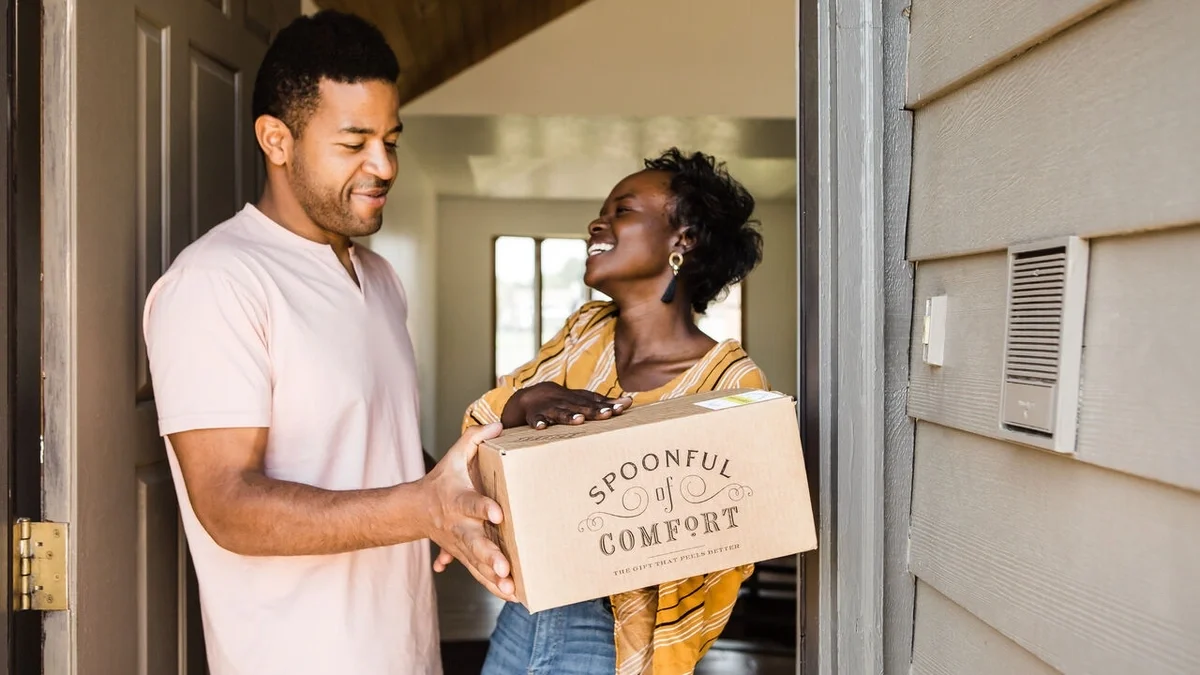 Couple standing together in an open doorway, smiling as they hold a Spoonful of Comfort gift box.