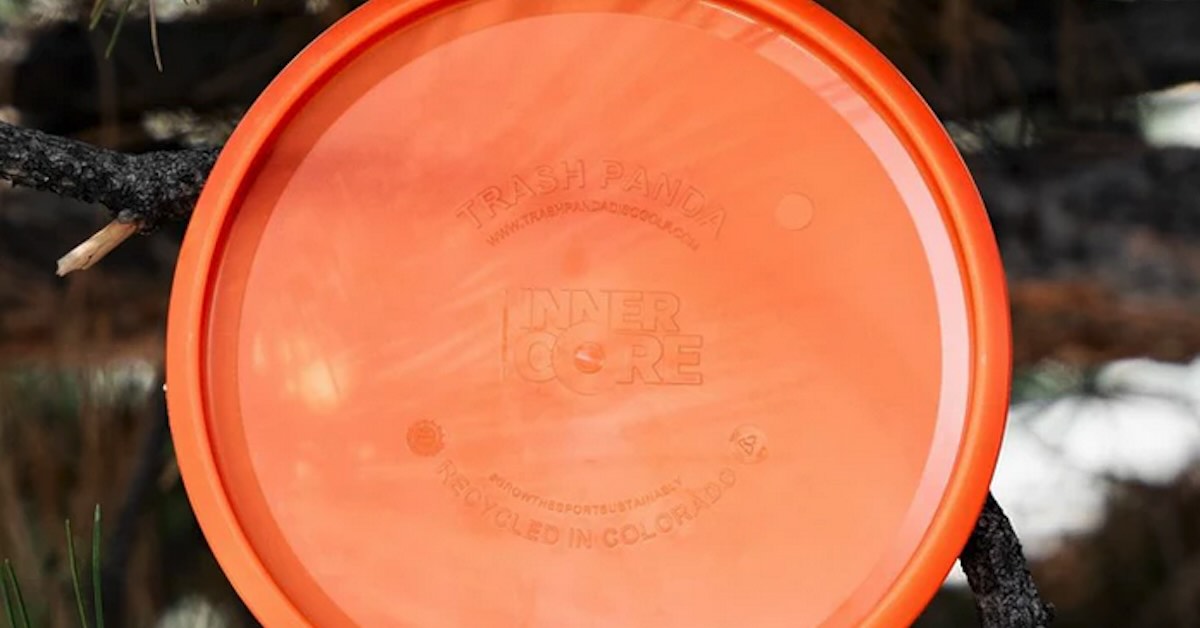 Bottom of an orange disc golf disc leaning on a small branch