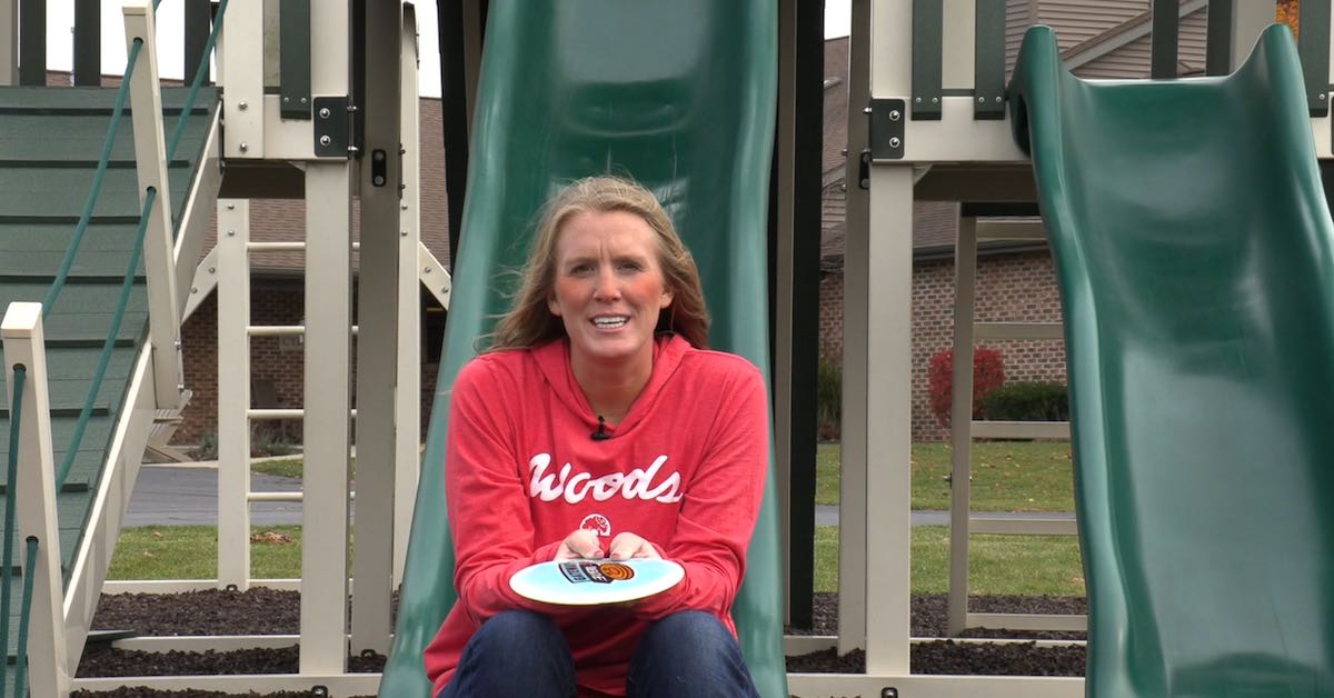 Woman in a red sweatshirt sits on the end of a lide holding a disc
