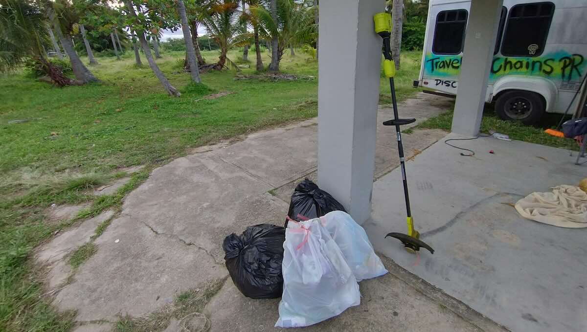 Trash bags, a weedeater, and a van on concrete in an outdoor area