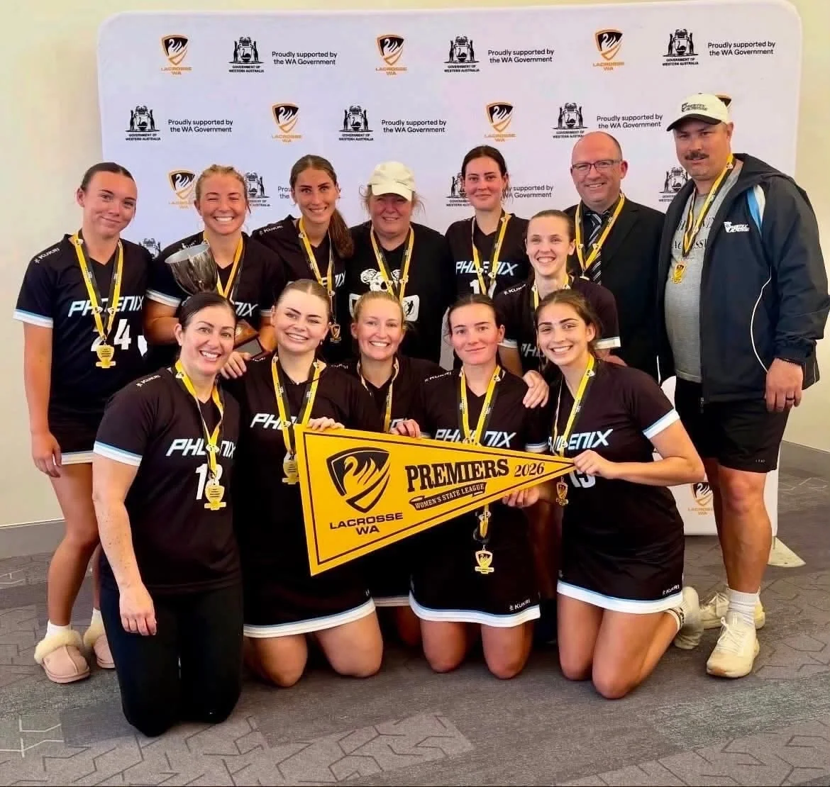 The Phoenix Lacrosse women's team holding a 2026 Premiers pennant