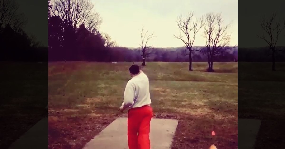 Chris Dickerson in a grainy photo on a tee pad lining up a throw while wearing white shirt and orange ski pants