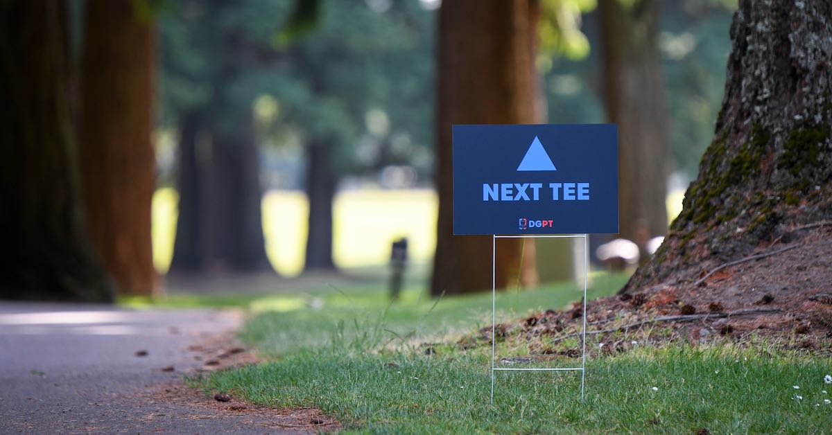 A small sign among large trees that says "Next tee."