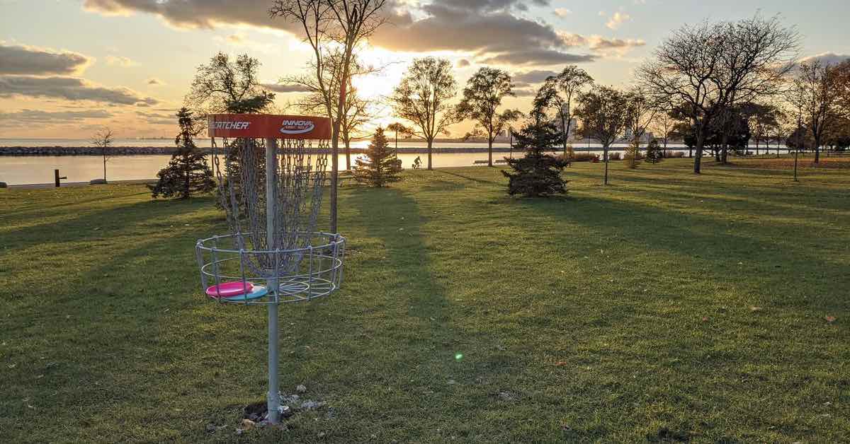 A red-banded disc golf basket in a park landscape near a waterfront