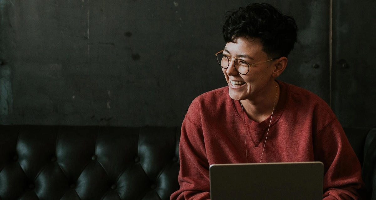 Person with short hair and glasses smiling while using laptop.
