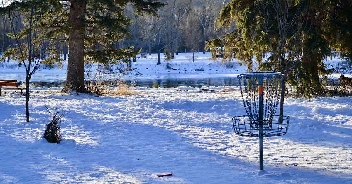 A disc golf basket in front of water in a snowy landscape